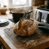 Steaming sourdough bread on wire rack with cast iron pot and oven mitt in background